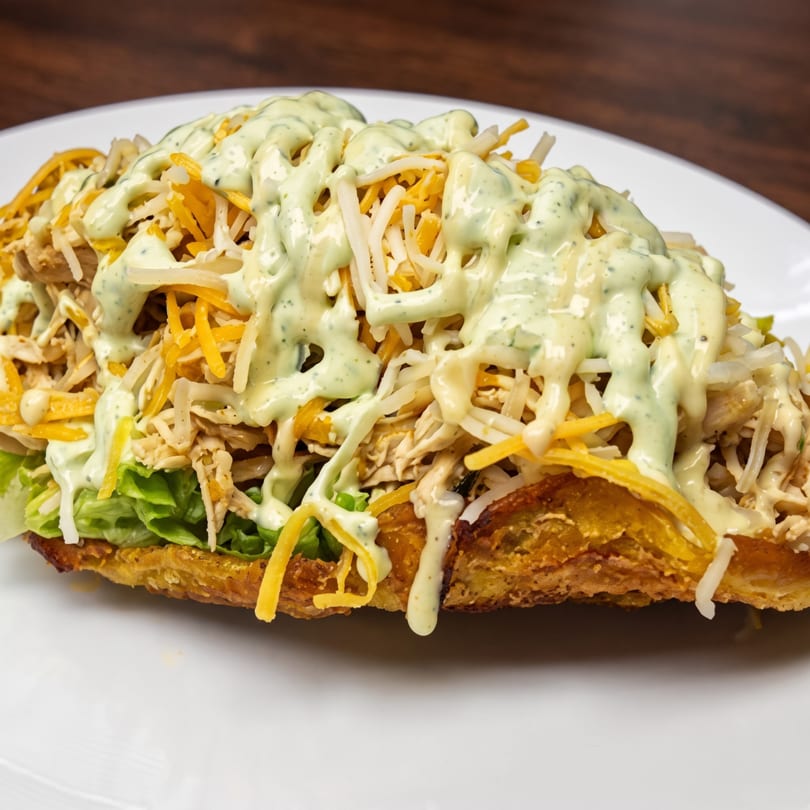 A croissant sandwich filled with shredded chicken, lettuce, cheese, and a creamy green sauce.