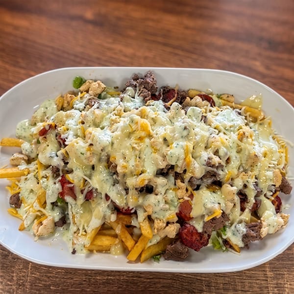 A large white platter filled with golden french fries, topped with various meats, cheese, and a creamy white sauce.