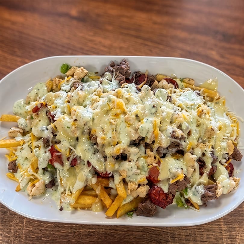 A large white platter filled with golden french fries, topped with various meats, cheese, and a creamy white sauce.